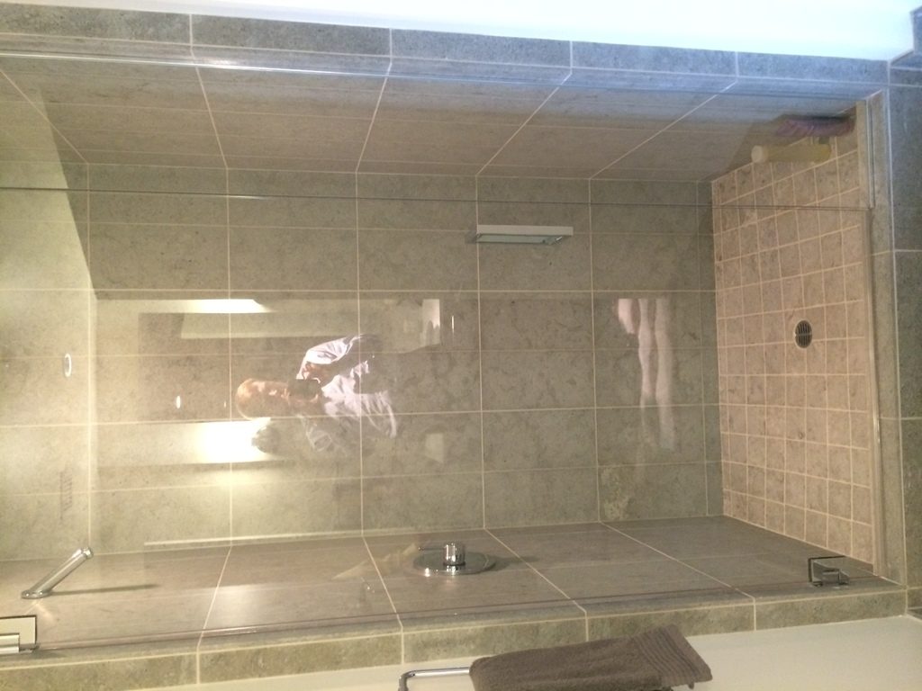 Walk-in shower with a glass panel and large beige stone tiles