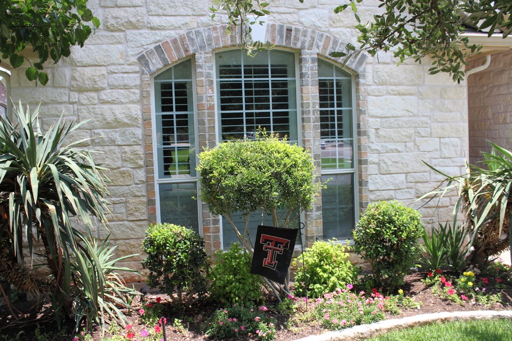 Stone house with tall arched windows framed by palms, shrubs and colourful flower beds