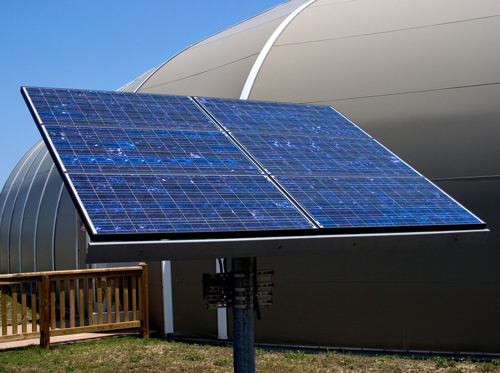 Tilted solar panel on a steel post under a clear blue sky